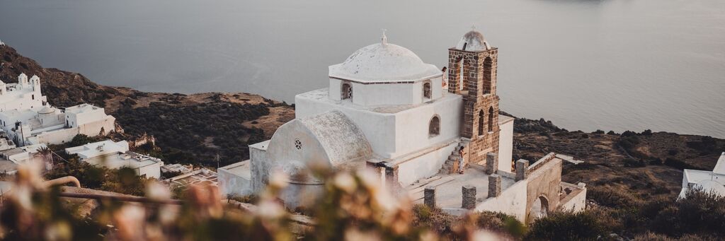Biela budova s kupolovitou strechou na vrchole kopca v Santorini, Grécko.