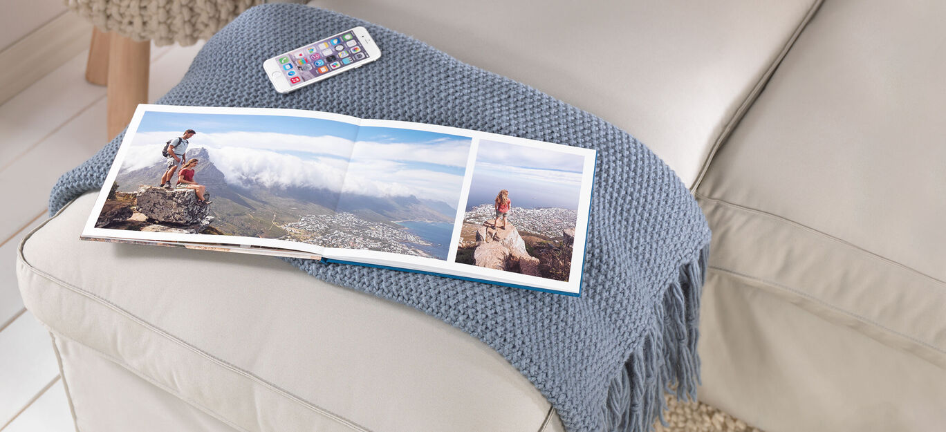 CEWE FOTOKNIHA leží na svetlej pohovke vedľa smartfónu.