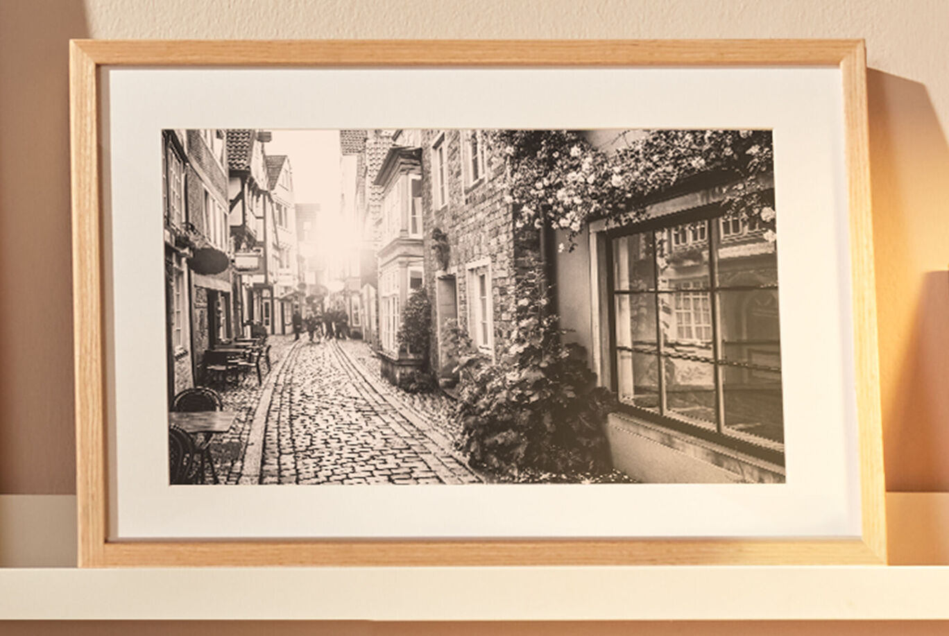 Čiernobiela fotografia dláždenej ulice s domami, v pozadí slnečné svetlo.