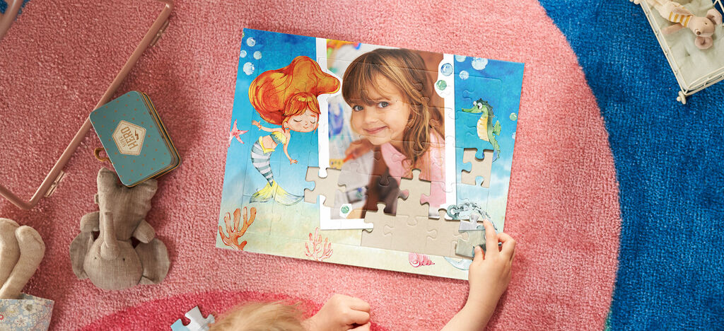 Dieťa sa hrá s puzzle na pestrofarebnom koberci. Motívy pod vodou s rybami a témou morskej panny.