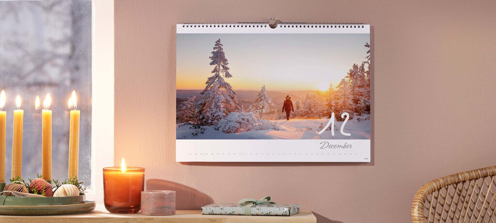 Adventný kalendár so sviečkami, vianočným stromčekom a teplou atmosférou. V pozadí je zimná krajina.