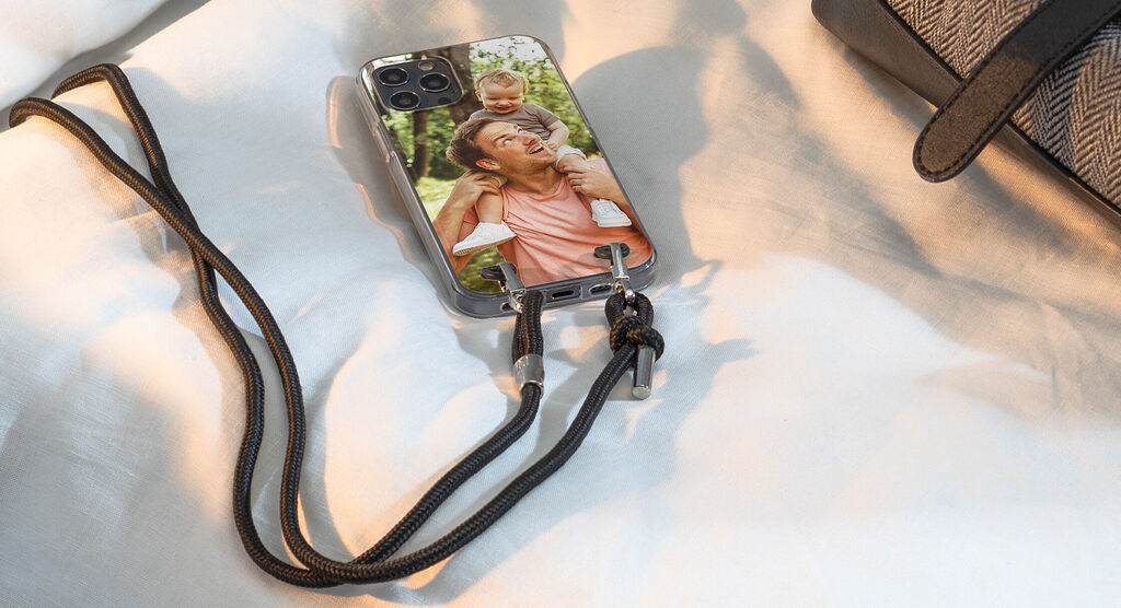 Smartfón s personalizovaným krytom zobrazujúcim veselú momentku otca s jeho dieťaťom, položený na svetlom podklade.
