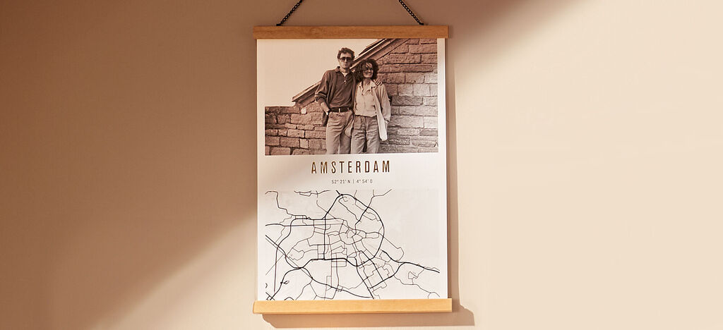 Čiernobiely obraz ukazuje pár pred stenou s nápisom „AMSTERDAM” a mapu mesta.