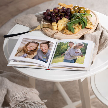 Otvorená fotokniha s rodinnými fotografiami a tanierom s hroznom, syrom a olivami na stole.