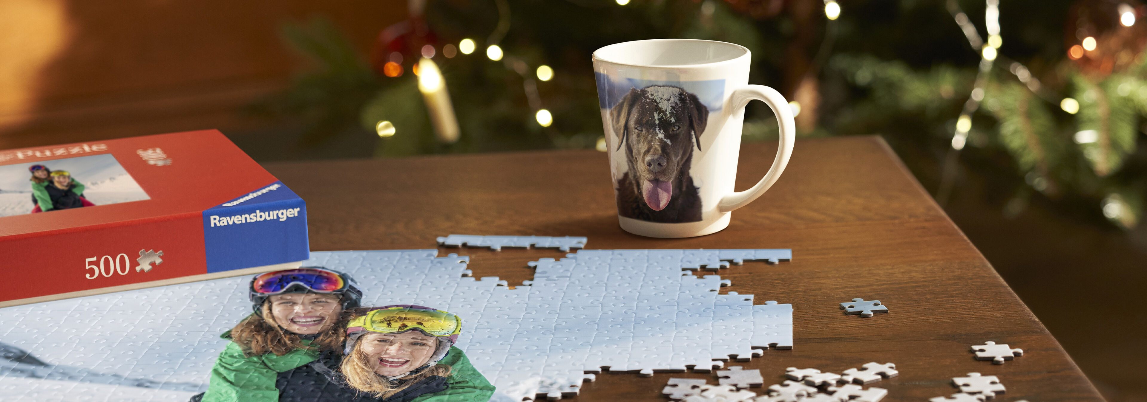 Puzzle a šálka s motívom psa na stole, obklopené vianočnými dekoráciami.