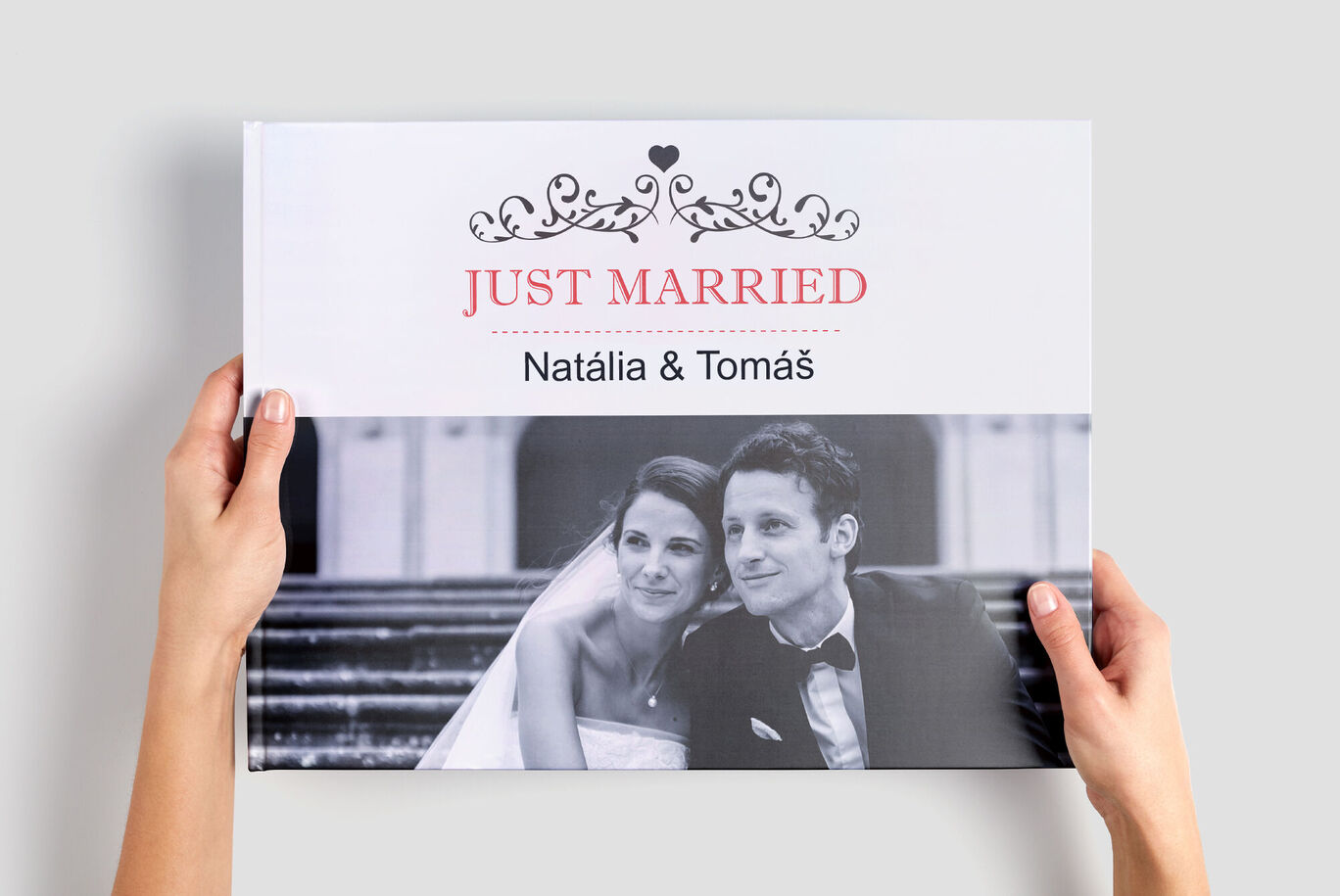 Dvaja ľudia držia CEWE fotoknihu s nápisom „Just Married“ a menami.