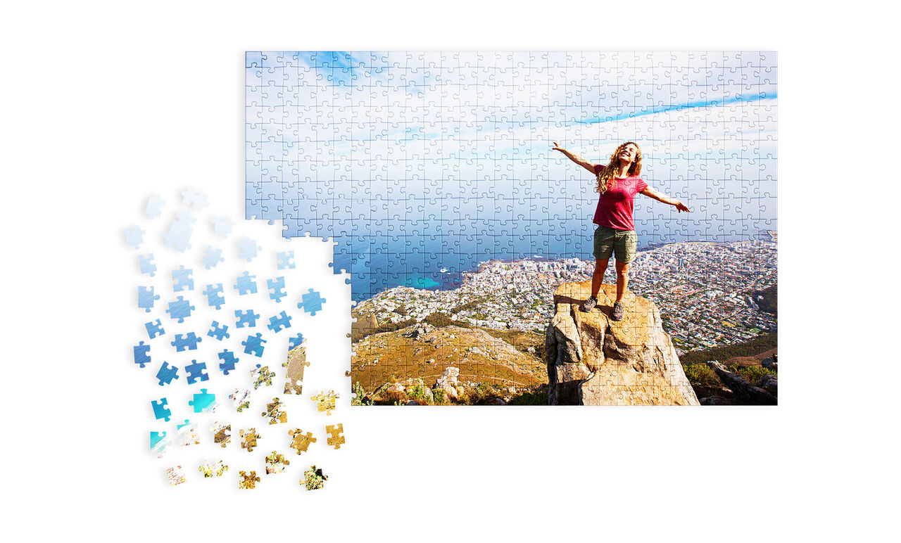 Osoba s rozpaženými rukami stojí na skale s výhľadom na pobrežie a more, obklopená dielikmi puzzle.