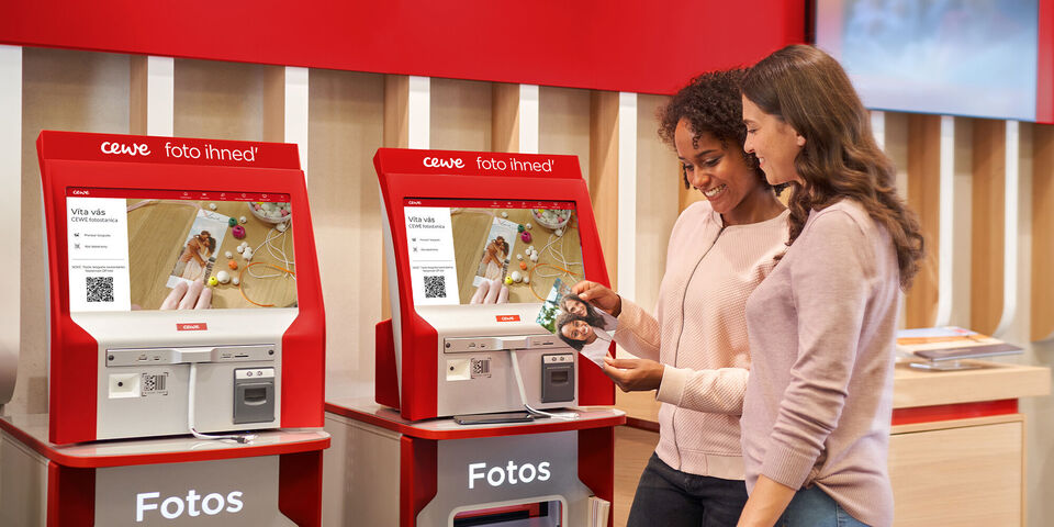 Dve ženy používajú CEWE foto inred automat na objednanie fotiek.