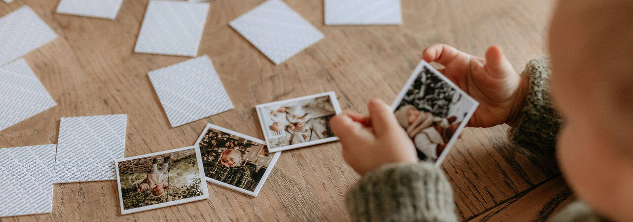 Dieťa drží fotky v rukách a pozerá na ne. Okolo sú ďalšie fotografie na drevenej podlahe.