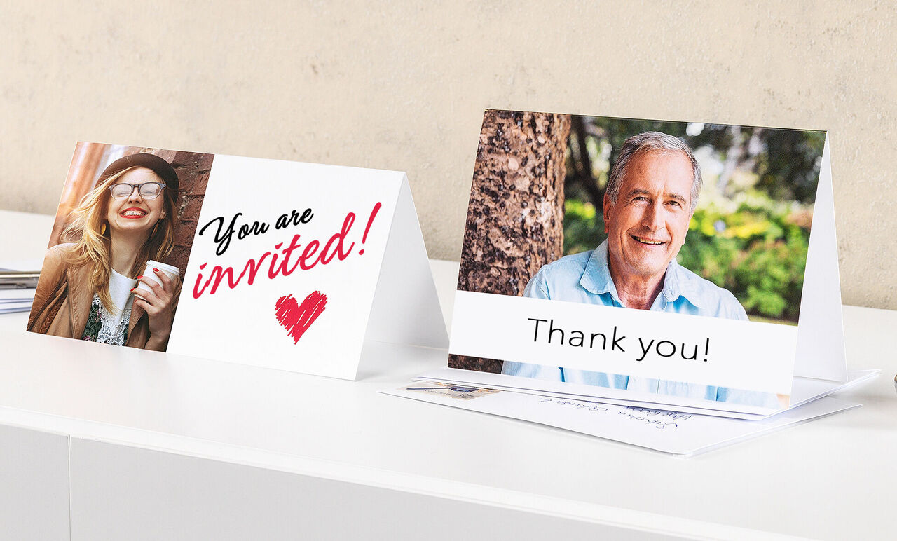 Dve prívetivé pohľadnice na stole. Jedna zobrazuje text 'You are invited!' farebnými písmenami, druhá 'Thank you!' pod obrázkom.